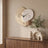 A wall clock and ceramic vase on and above a walnut sideboard against a warm plaster wall