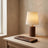 A walnut-finish wrist rest and desk lamp on a white oak desk against a warm plaster wall