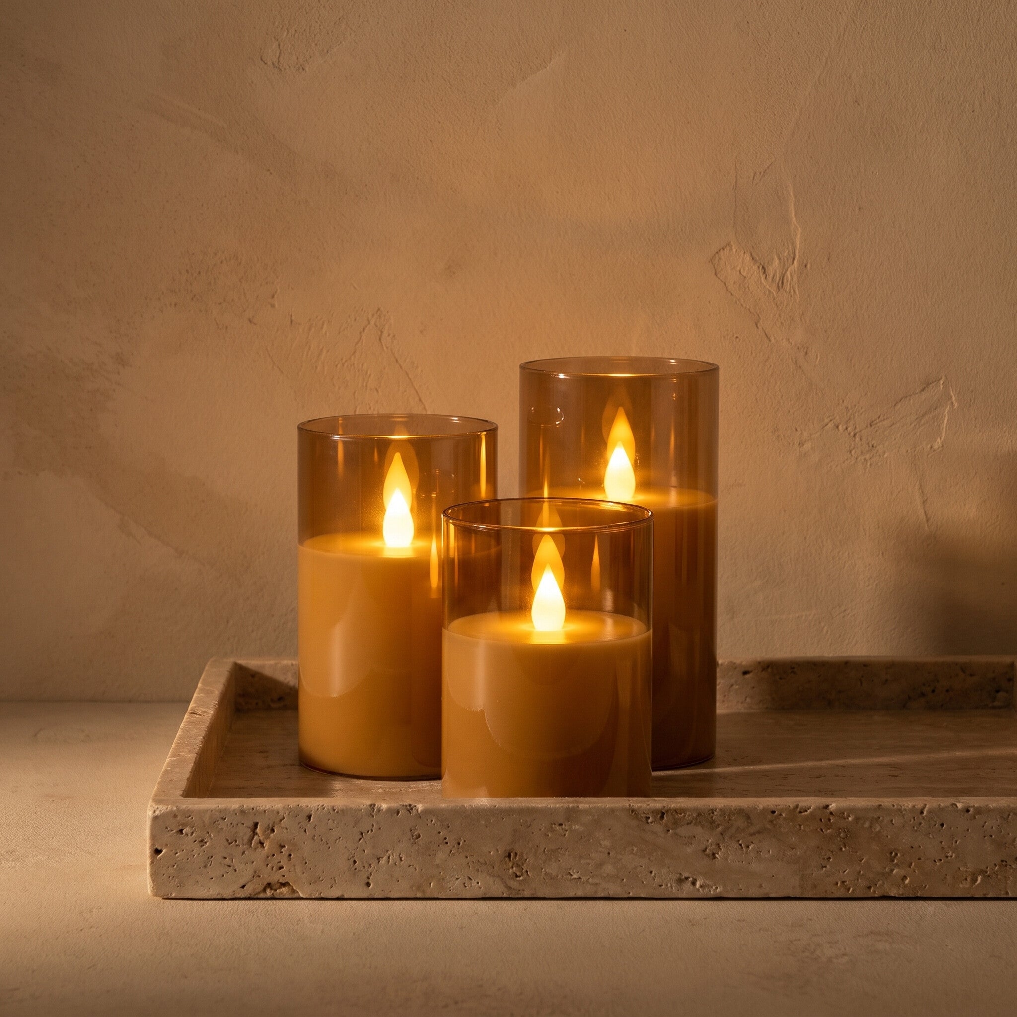 Three flameless LED candles lit on a travertine tray in low evening light