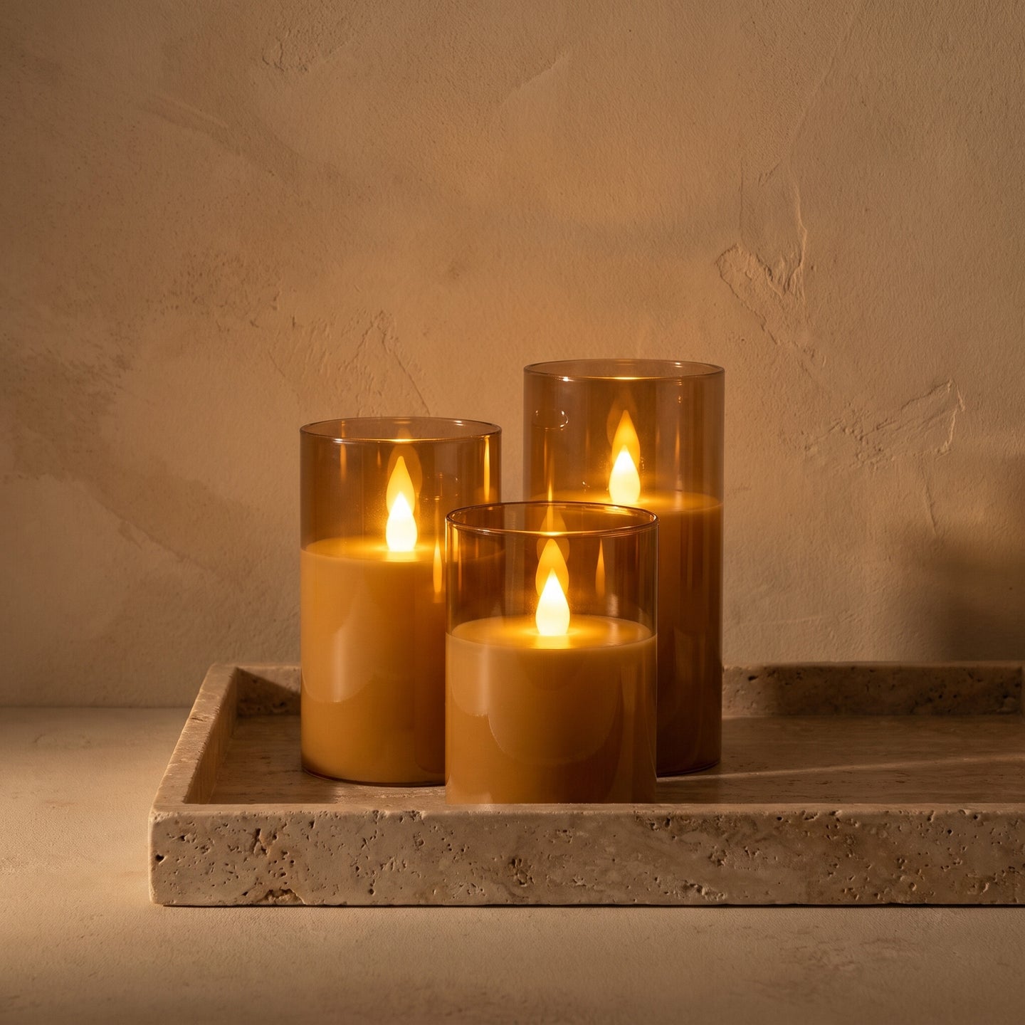 Three flameless LED candles lit on a travertine tray in low evening light