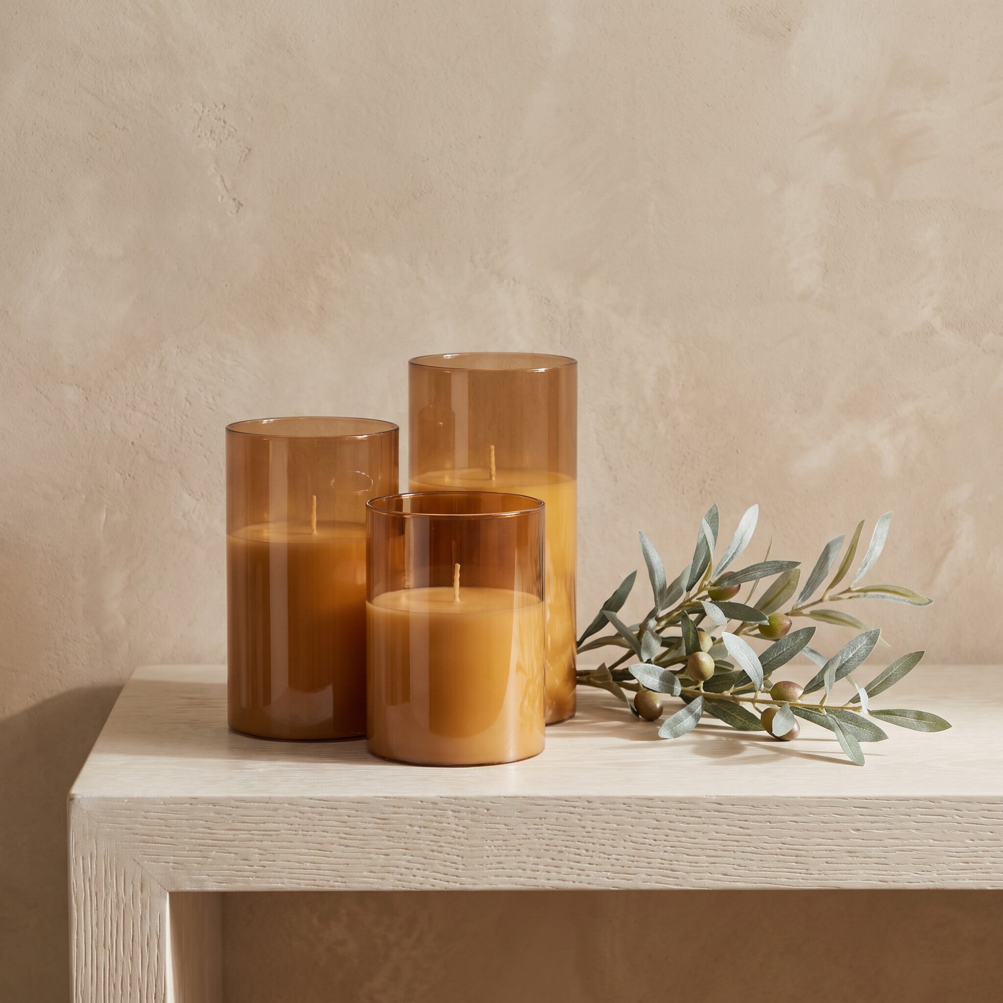 Three flameless LED candles unlit on a white oak console beside an olive branch