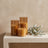 Three flameless LED candles unlit on a white oak console beside an olive branch