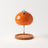 Glass candle warmer lamp in orange, shown alone with an empty base on a plain off-white background