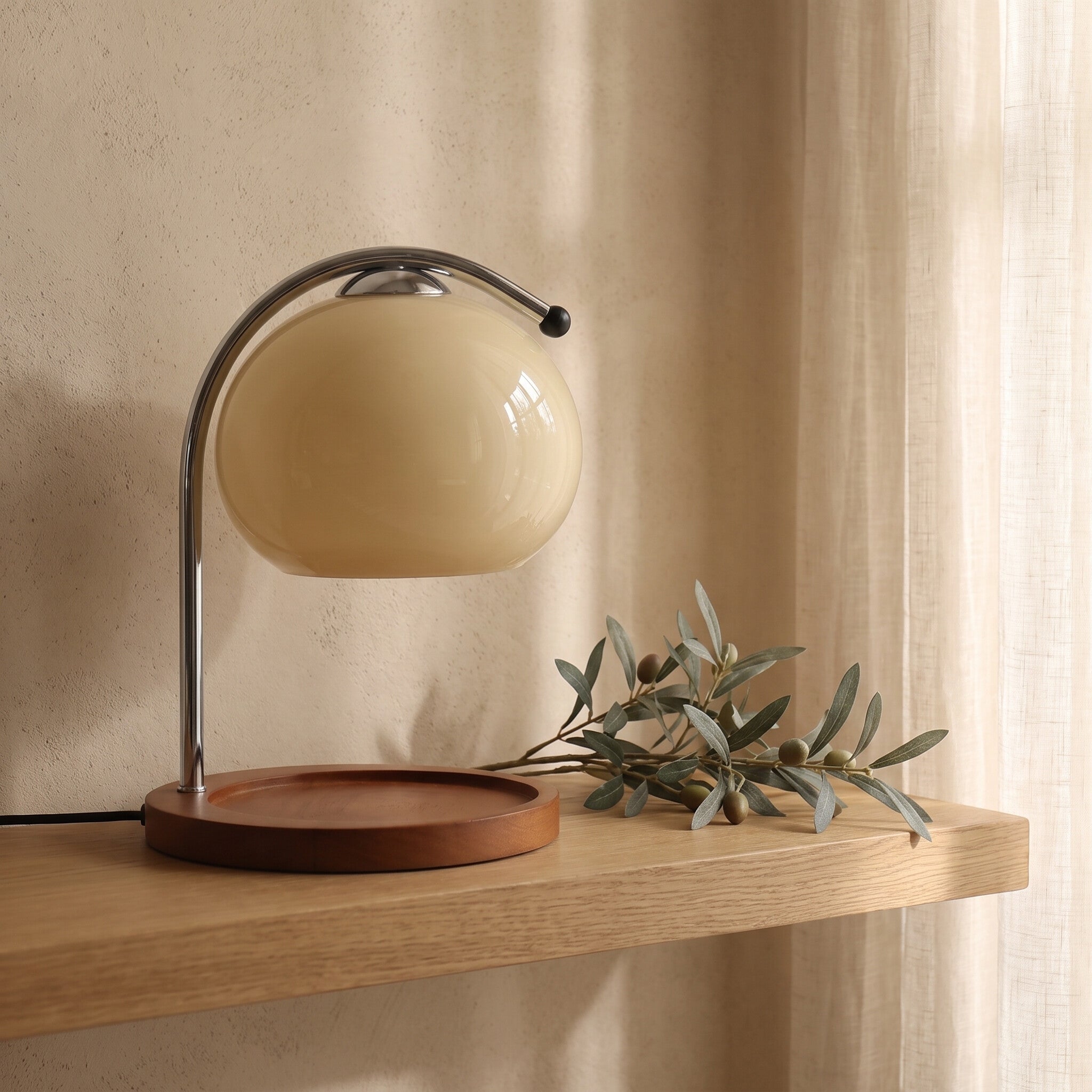 Glass candle warmer lamp switched off on a white oak shelf beside an olive branch in daylight