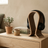 Wooden headphone stand with black headphones on a wooden side table next to a sofa and books.
