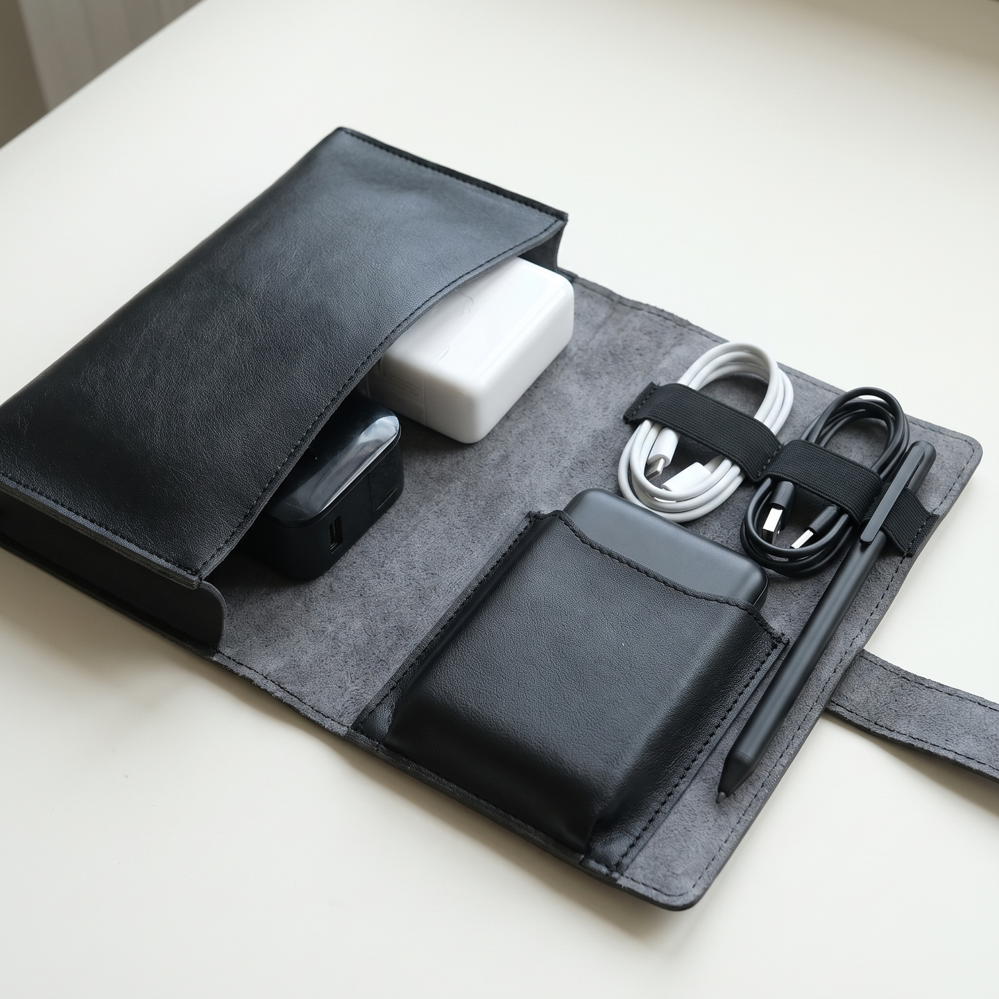 Close-up of the PU Leather Tech Organizer Case in black, opened flat showing the charger compartment, cable loops, and pen loop