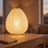 Rice Paper Lantern Table Lamp, lit, on a desk beside a notebook
