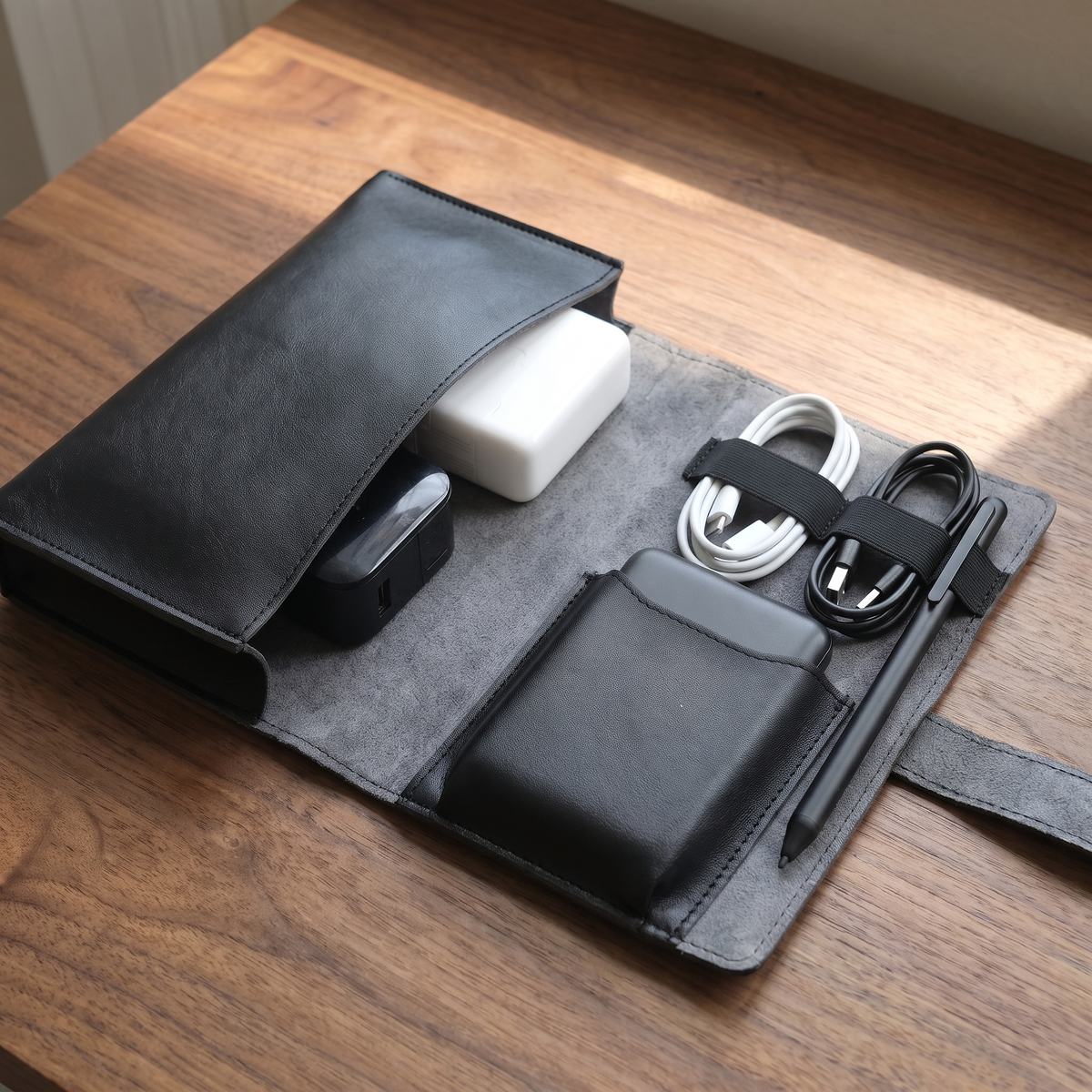 PU leather tech organizer case, black finish, open on a desk with charging cables secured in the loops
