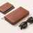 PU leather tech organizer case, brown finish, zipped closed in its folded travel form beside a passport and sunglasses