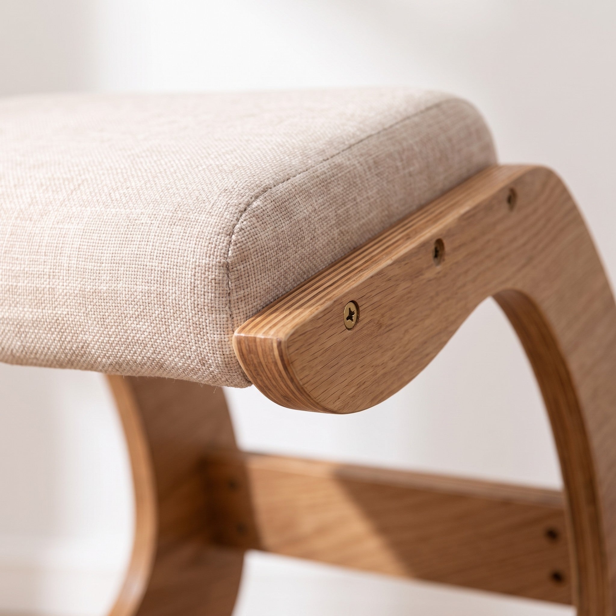 Close-up of the oatmeal fabric seat cushion meeting the light white oak frame of the Ergonomic Rocking Kneeling Chair.
