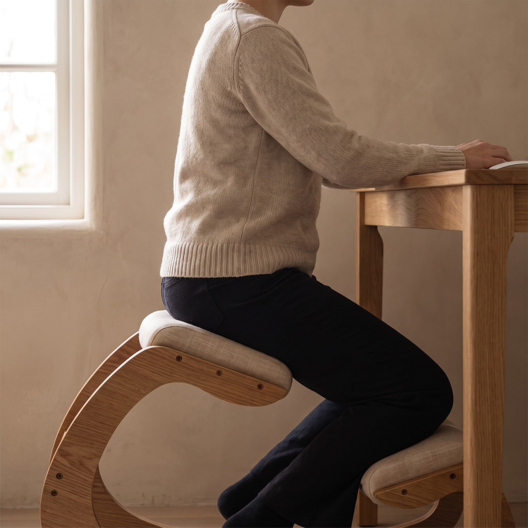 Side view of a person seated on the Ergonomic Rocking Kneeling Chair at a desk, weight forward on the seat pad with shins on the lower pad.