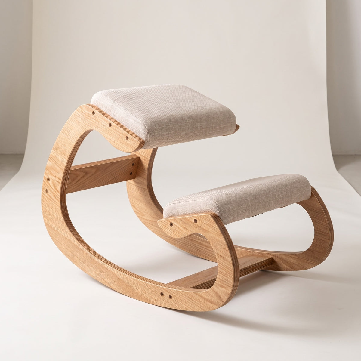 Ergonomic Rocking Kneeling Chair in light white oak with oatmeal cushions, shown at a three-quarter angle on an off-white studio backdrop.