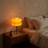 Orange Macaron Glass Table Lamp lit at night on a walnut nightstand beside a bed with oatmeal linen bedding.