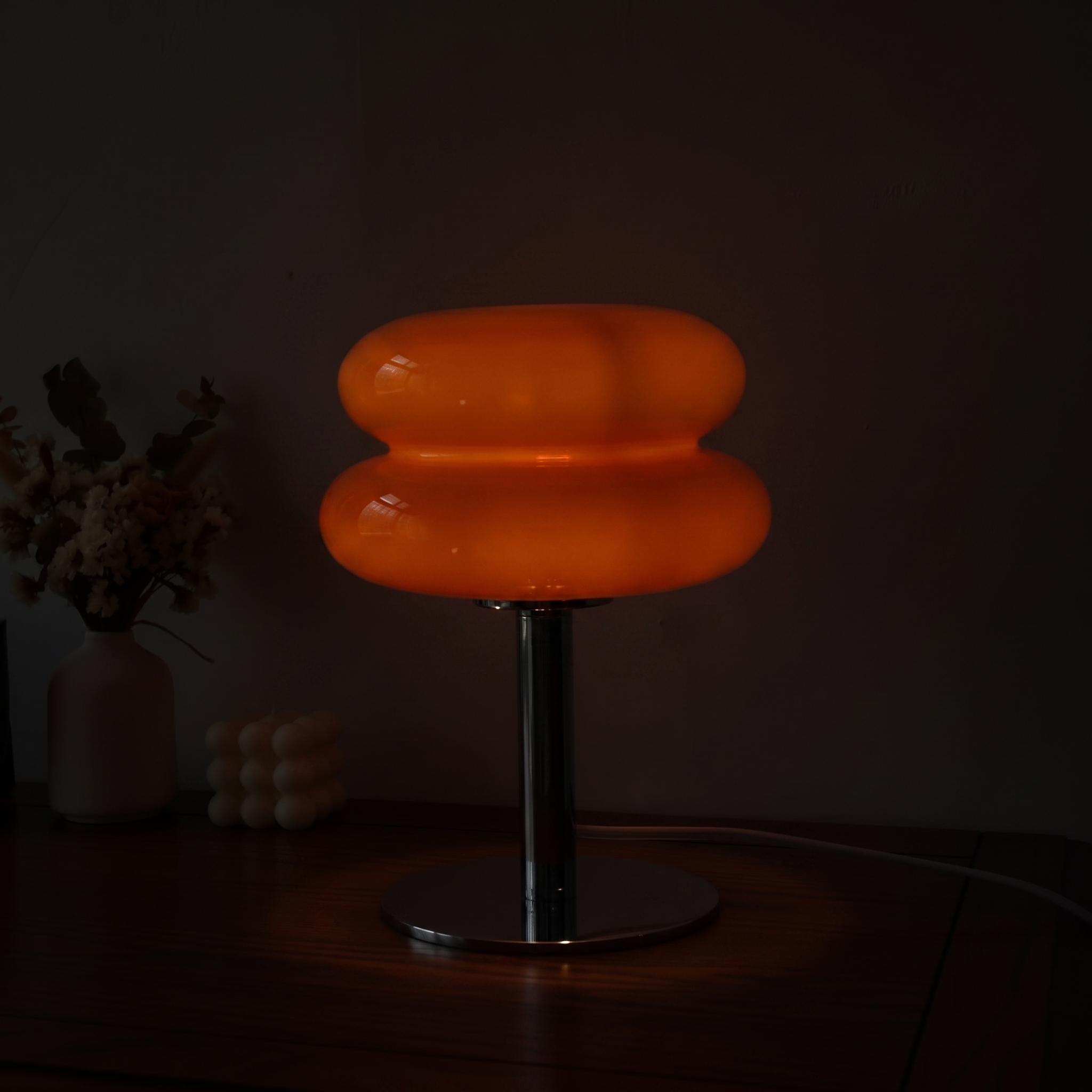 Orange Macaron Glass Table Lamp at its lowest dim setting in a dark room, a faint warm glow held inside the glass.