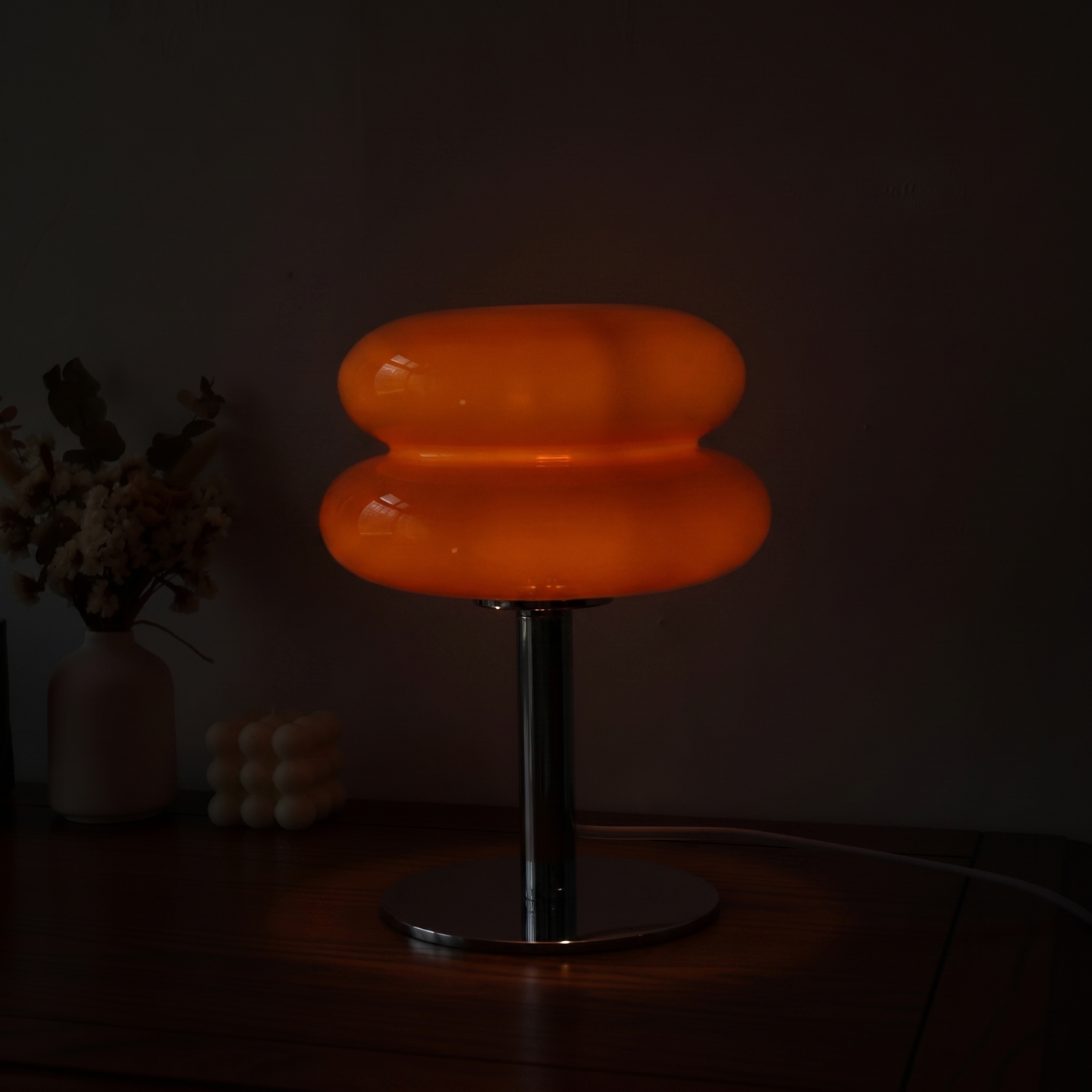 Orange Macaron Glass Table Lamp at its lowest dim setting in a dark room, a faint warm glow held inside the glass.