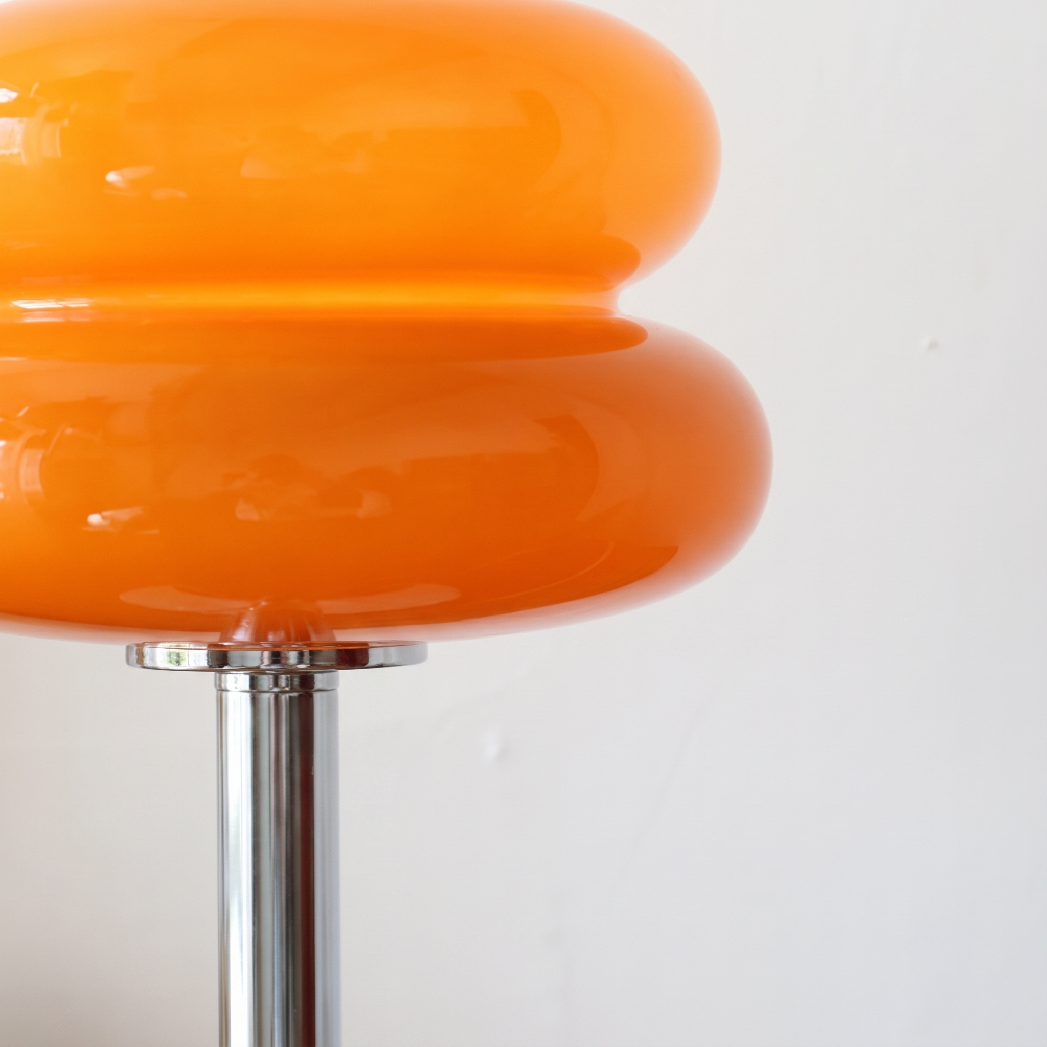 Close-up of the orange Macaron Glass Table Lamp, showing the seam where the two glass discs meet above the polished chrome stem.