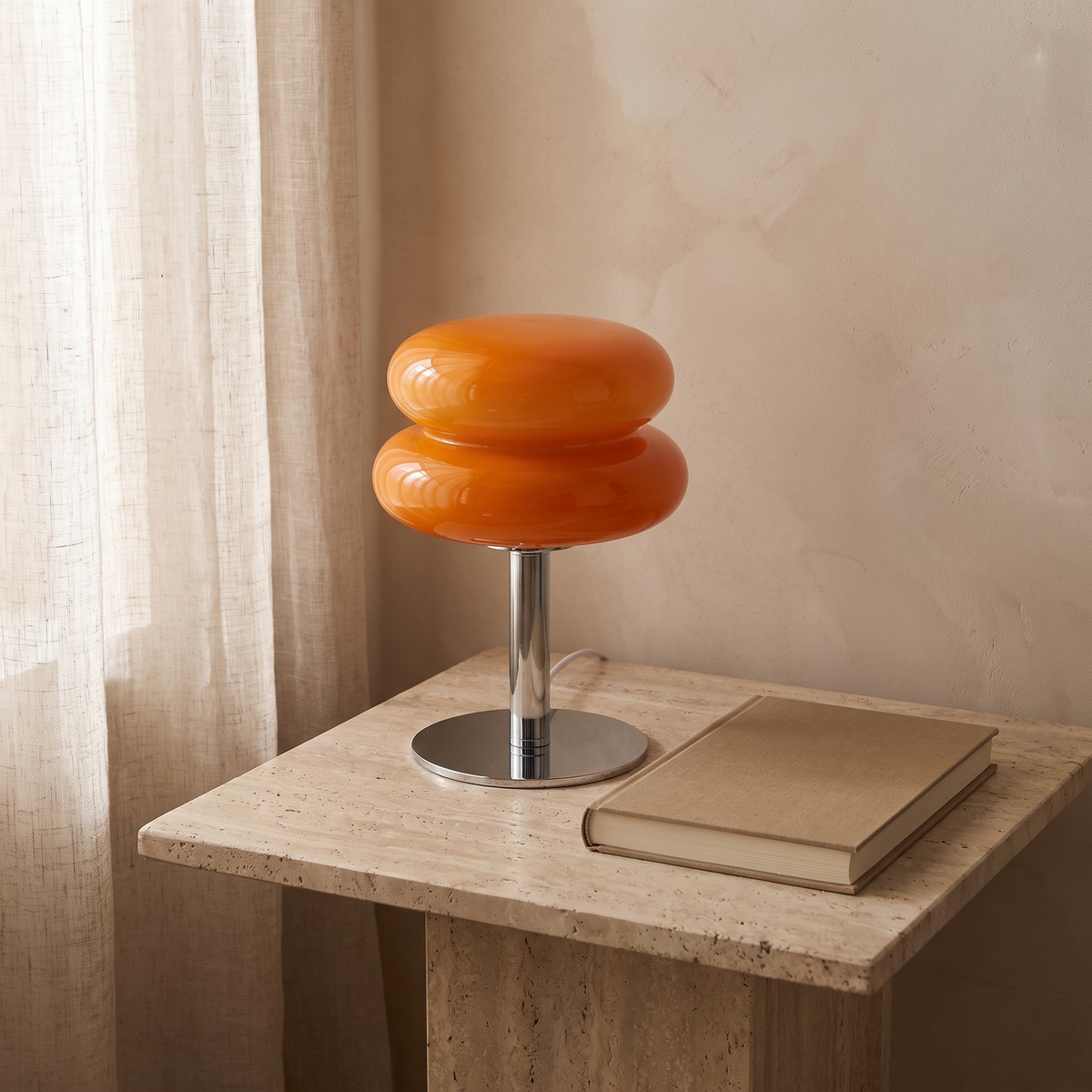 Orange Macaron Glass Table Lamp switched off on a travertine nightstand beside a hardback book, showing its 11 inch height.