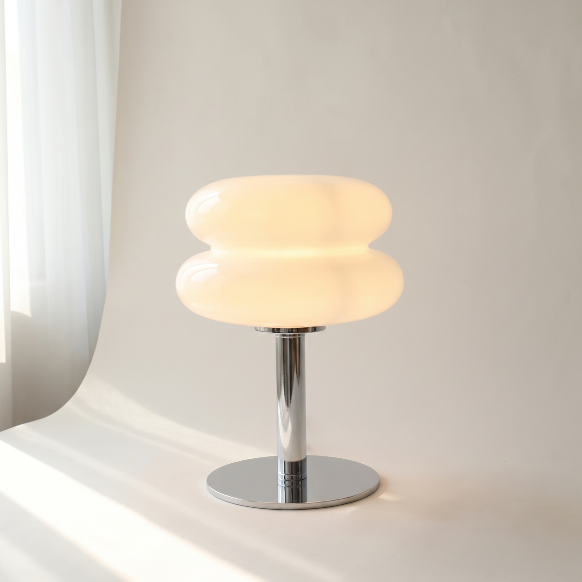White Macaron Glass Table Lamp lit on an off-white studio backdrop, showing its two stacked glass discs and round chrome base.