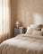 Fabric drawer nightstand in gray, styled beside a bed with oatmeal linen bedding in a warm plaster-walled bedroom