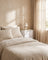 Fabric drawer nightstand in white, styled beside a bed with oatmeal linen bedding in a warm plaster-walled bedroom