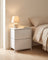 Fabric drawer nightstand in white in a minimalist bedroom with a lamp and book on top, white oak flooring
