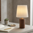 Table lamp with pleated shade on a desk next to an open book and small plant.
