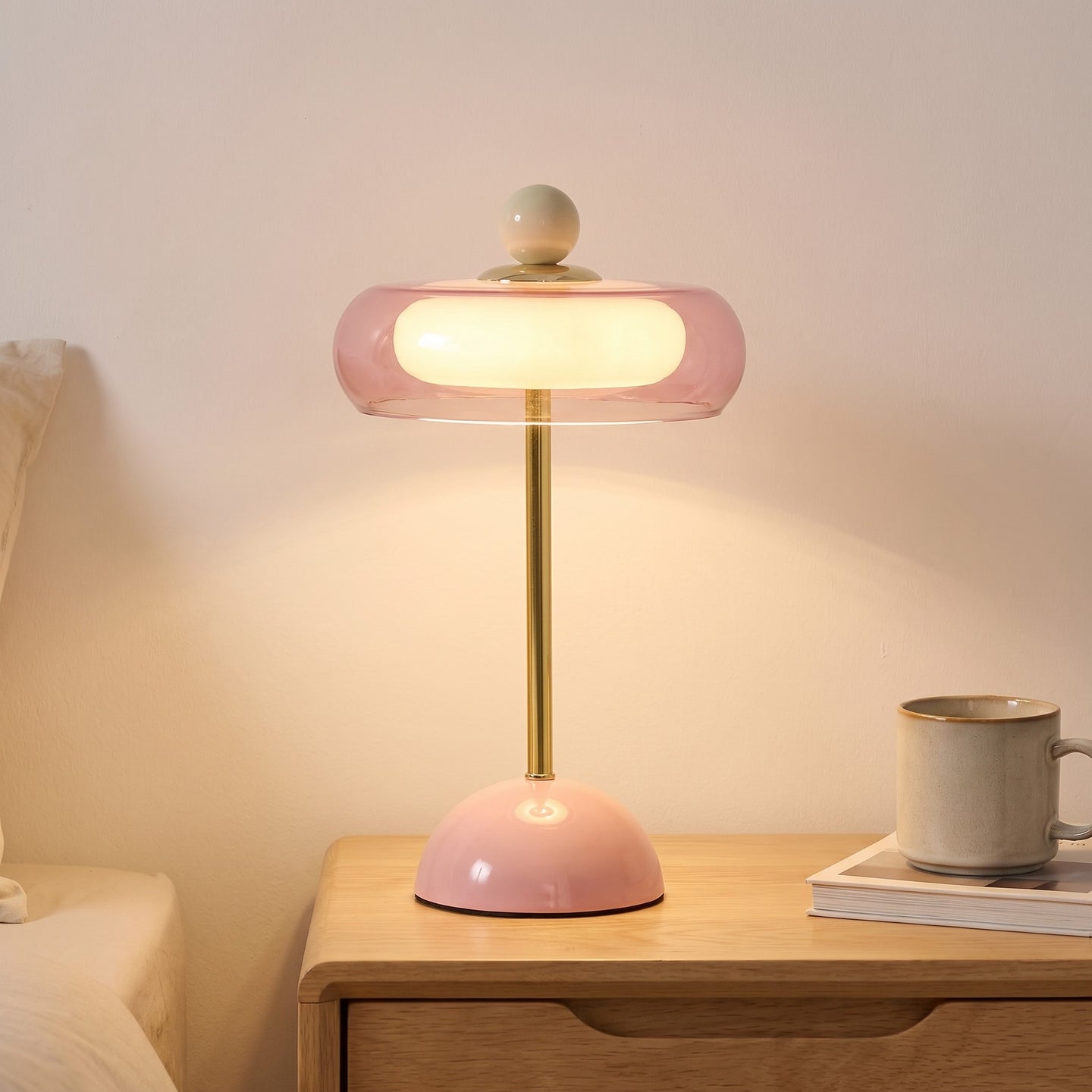 Pink glass ring table lamp lit on a bedside table