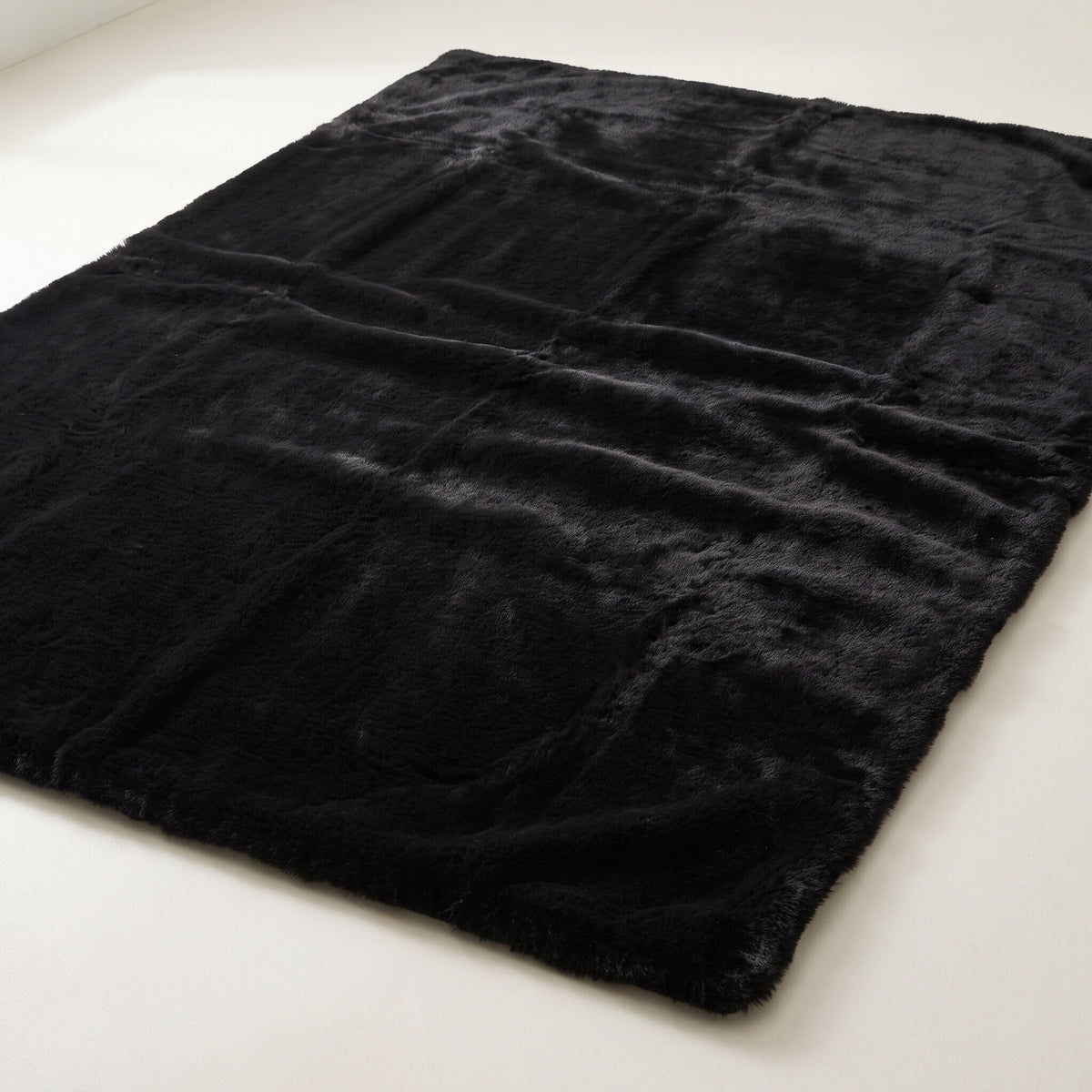 Plush faux-fur area rug in solid black on a plain off-white background