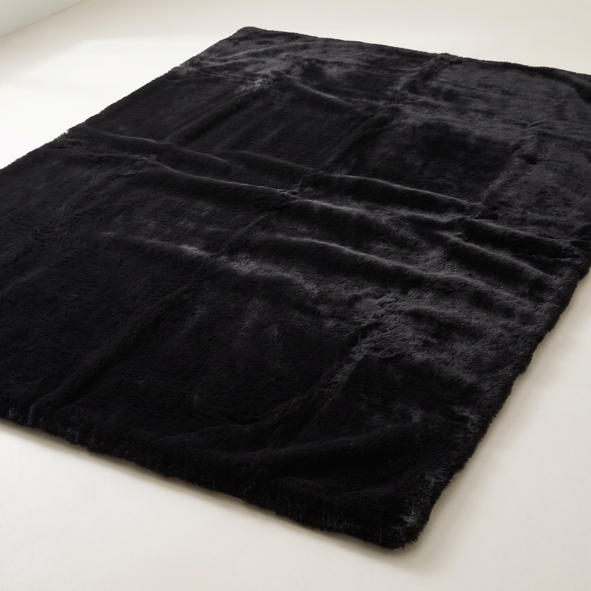 Plush faux-fur area rug in solid black on a plain off-white background