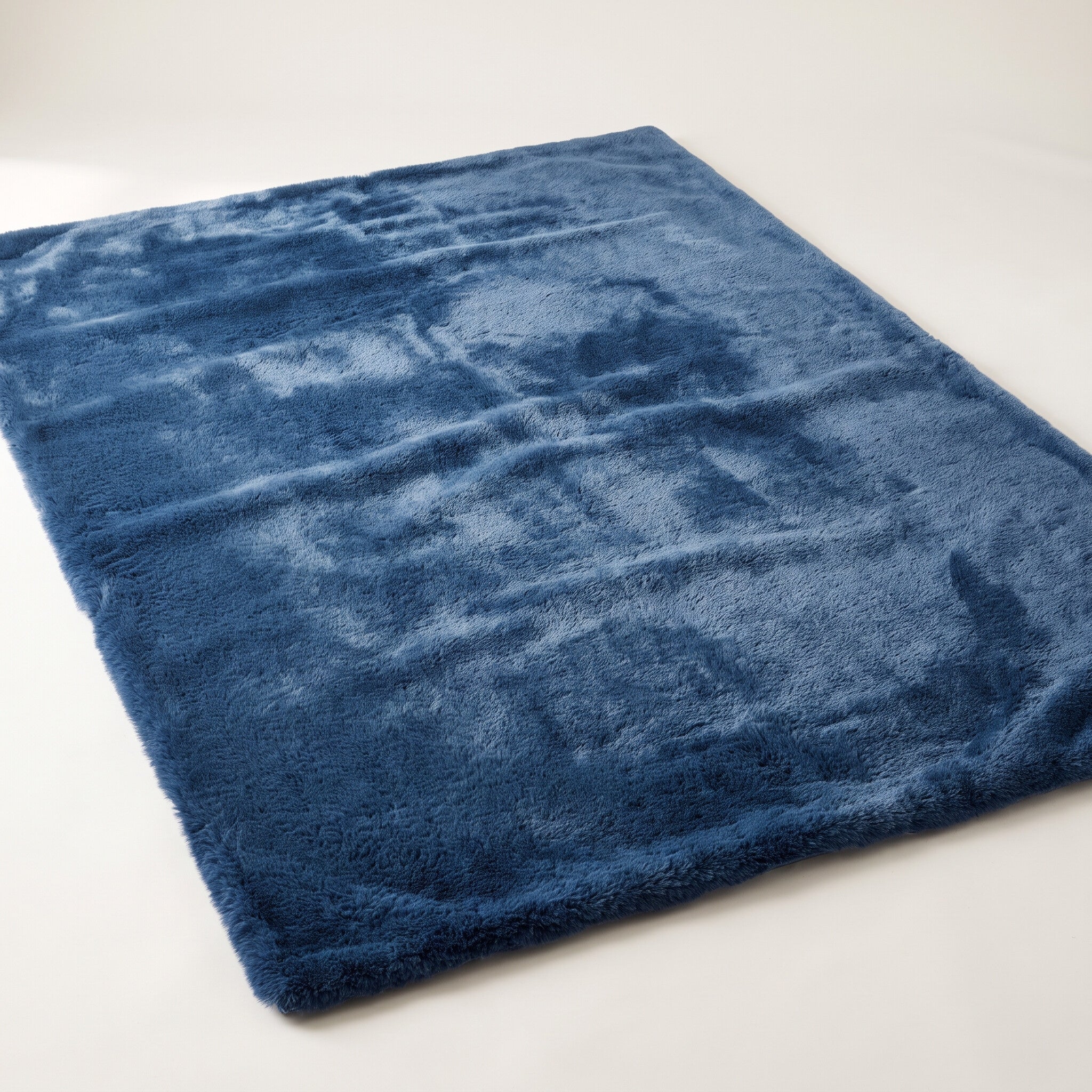 Plush faux-fur area rug in mottled deep blue on a plain off-white background