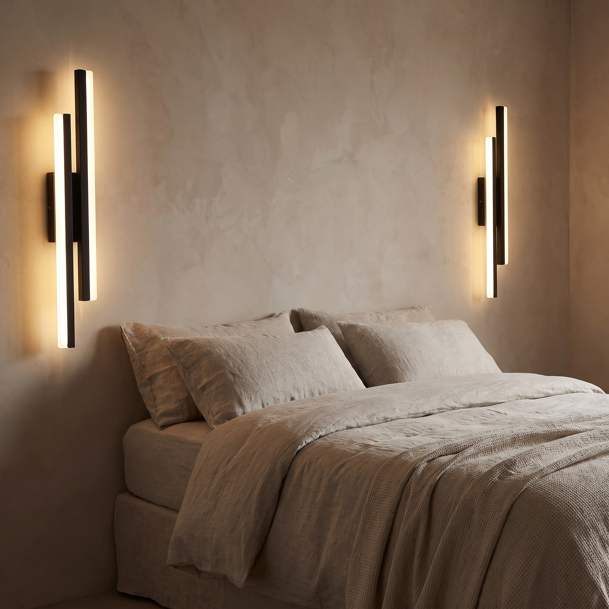 A left- and right-facing pair of slim sconces flanking a linen bed