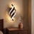Spiral LED wall sconce lit above a walnut nightstand in evening light