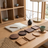 Wooden coasters and trays on a wooden table with a book and lamp in a room with large windows.
