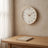 Cream Wood Frame Silent Wall Clock hanging on a plaster wall above a white oak desk in daylight.