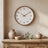 Brown Wood Frame Silent Wall Clock hanging on a limewash plaster wall above a kitchen counter with ceramic pieces.